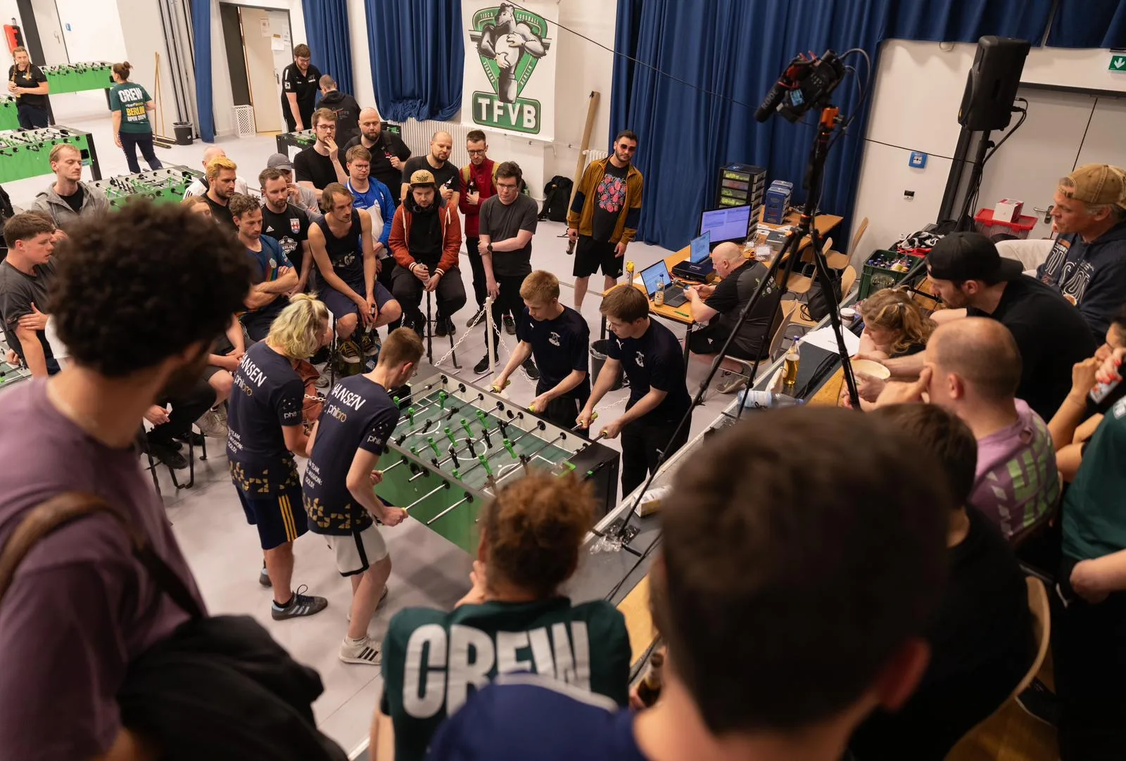 Dichte Zuschauermenge rund um einen Kicker-Tisch beim Turnier-Finale – Kameras, Spannung, Gemeinschaft